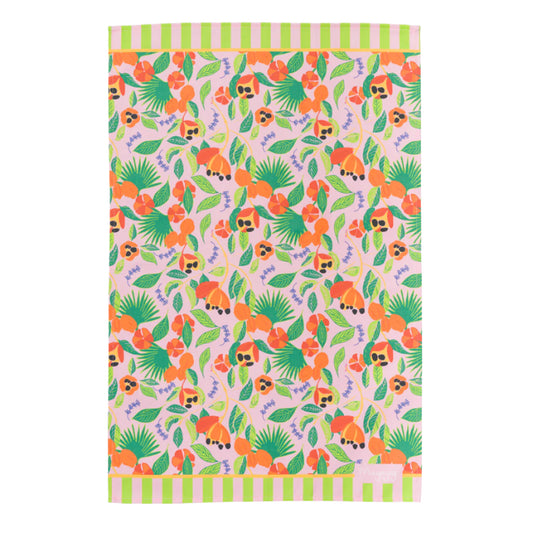 Flat lay colourful cotton tea tea towel in hand illustrated ackee print, with pink background, green leaves and orange ackee and lilac thyme leaves with hanging loop by Mayajoy