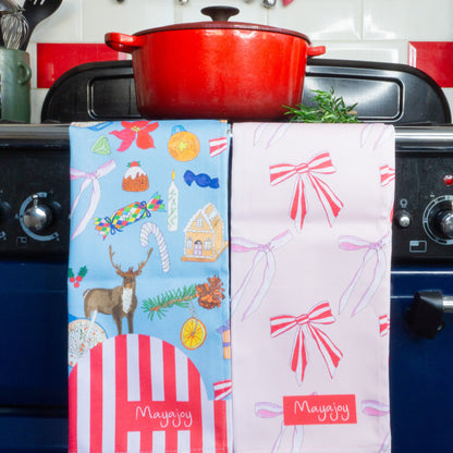 Pair of Christmas cotton tea towels in Christmas nostalgia and Xmas bows. Blue nostalgic hand drawn illustrations and pink candy stripe bows