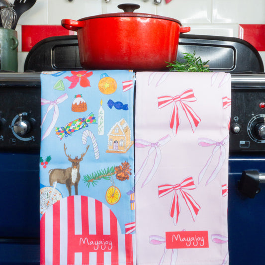 Pair of Christmas cotton tea towels in Christmas nostalgia and Xmas bows. Blue nostalgic hand drawn illustrations and pink candy stripe bows