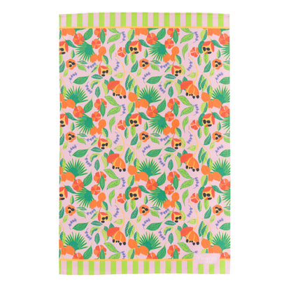 Flat lay colourful cotton tea tea towel in hand illustrated ackee print, with pink background, green leaves and orange ackee and lilac thyme leaves with hanging loop by Mayajoy 