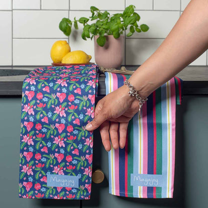 Colourful Striped tea towel in navy blue, pink and green hanging on edge of kitchen cabinet