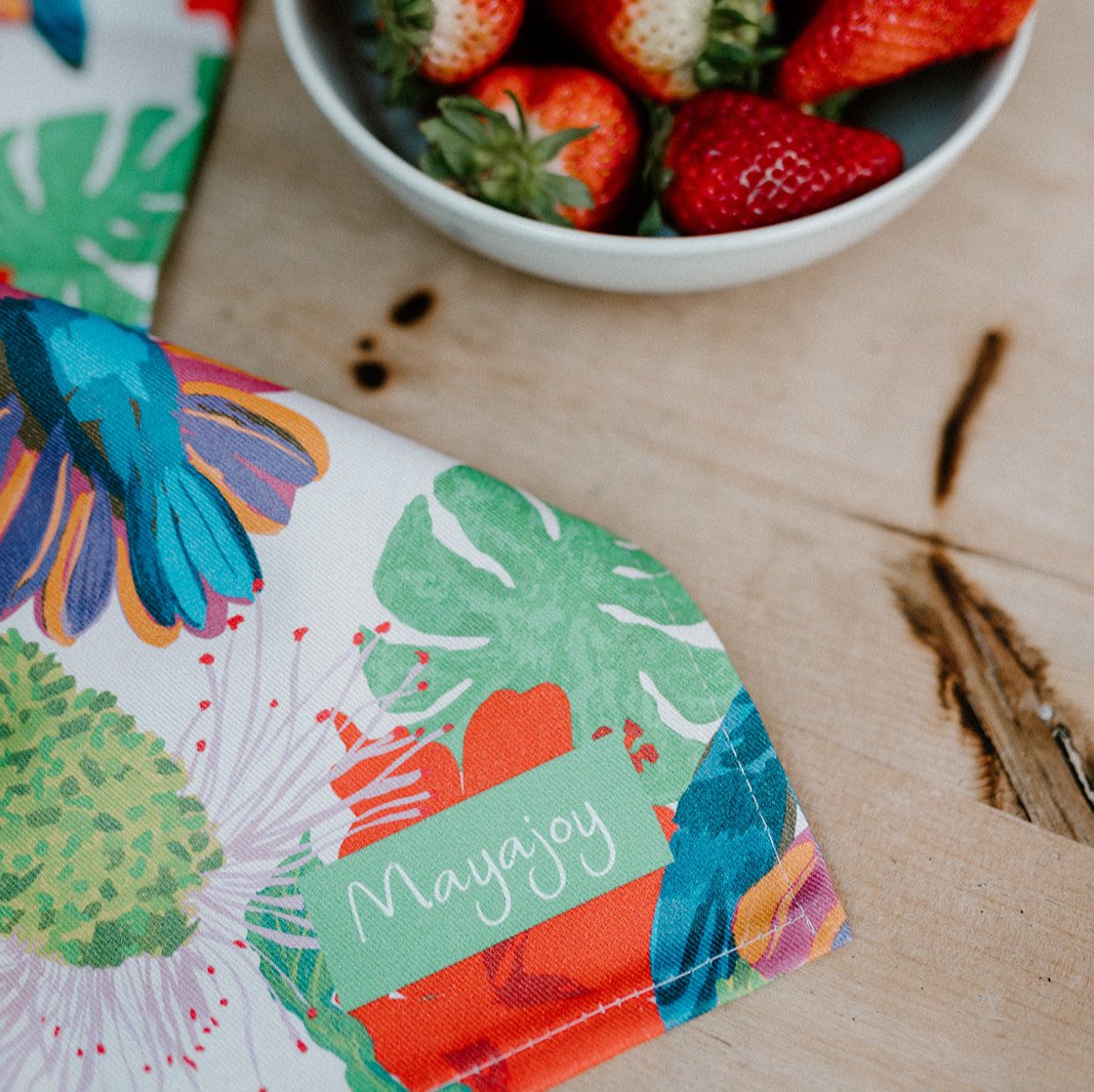 Colourful cotton tea towel with hand illustrated hummingbird design with pink background, pink, blue and green, styled next to a bowl of red strawberries 