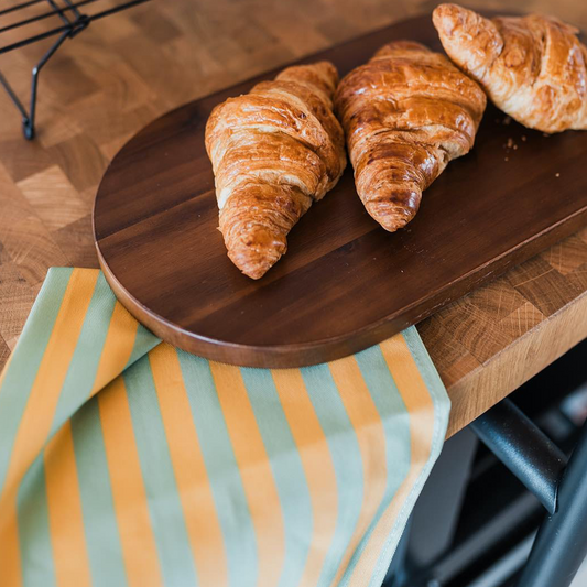 Yellow and green paradise stripe, colourful cotton tea towel with purple edge by mayajoy, styled with 3 croissants in kitchen.