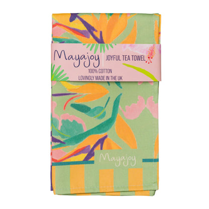 Mayajoy colourful cotton tea towel in paradise design, featuring orange bird of paradise flower with pink, green and purple, folded with coral belly band and words “joyful tea towel”.